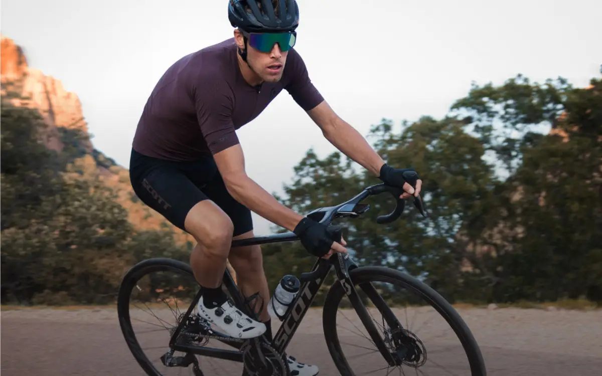 A road cyclist riding past rocky terrain and trees.