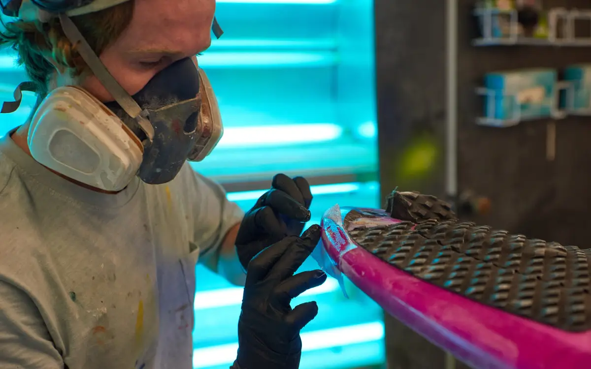 A surfboard repairer working on the rail of a board at Melbourne Surfboard Shop.
