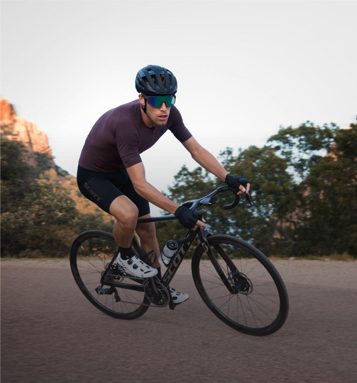 A road cyclist riding past rocky terrain and trees.