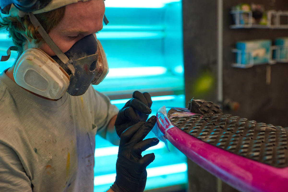 A surfboard repairer working on the rail of a board at Melbourne Surfboard Shop.